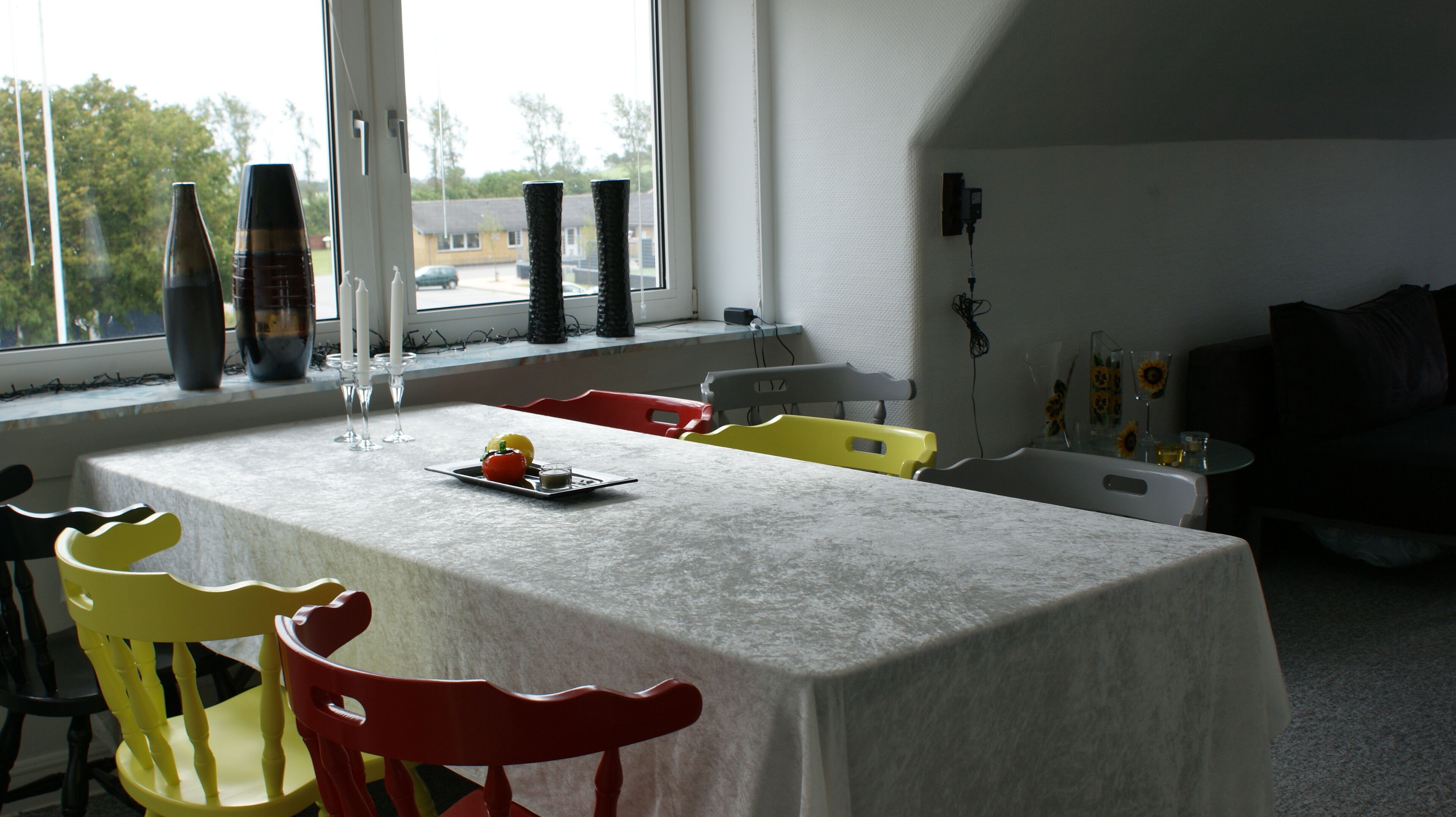 A dining area with a table set for two, chairs, and a window with a view of the outside.