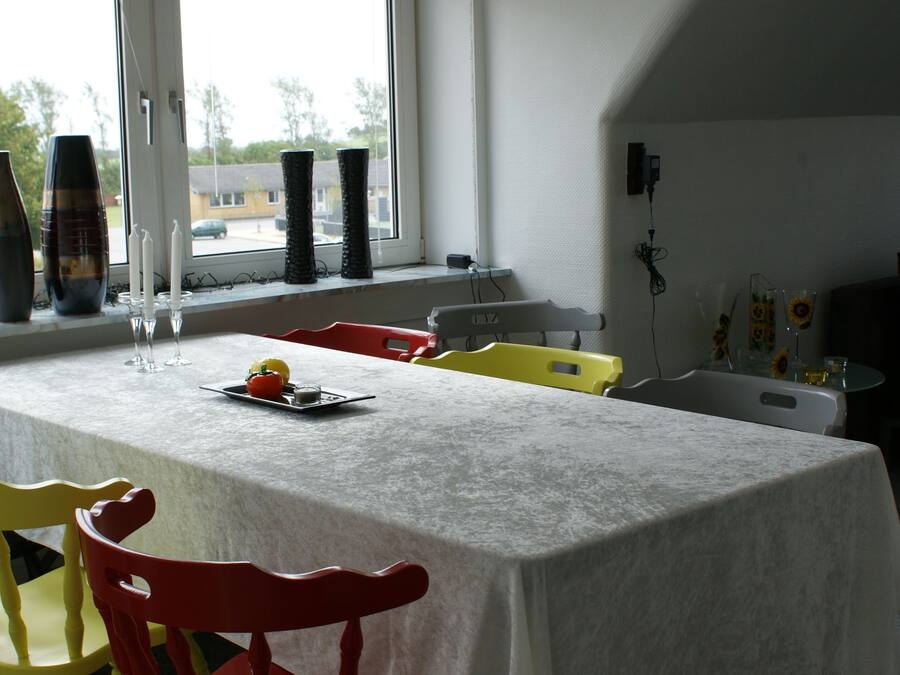 A dining area with a table set for two, chairs, and a window with a view of the outside.