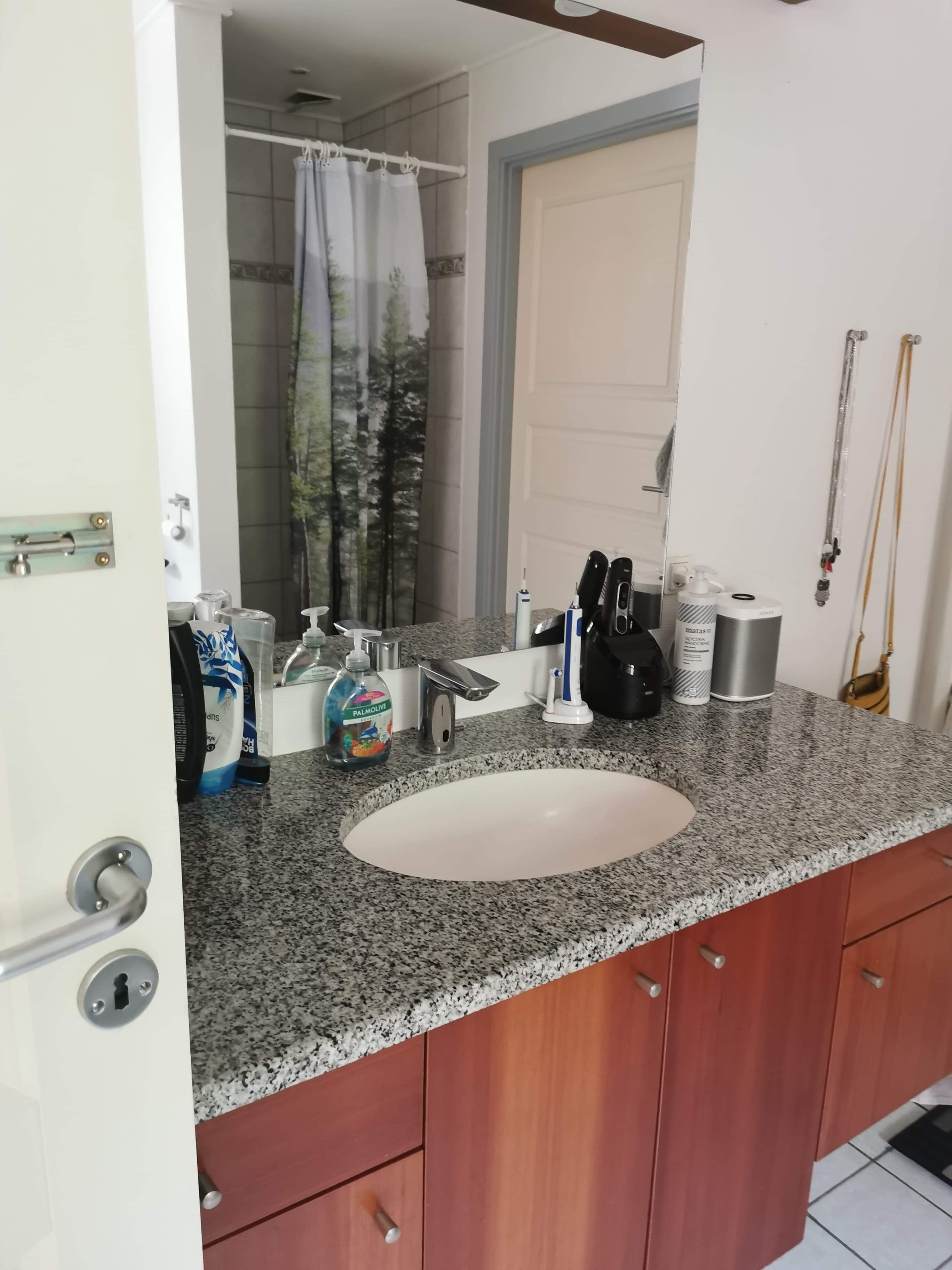 Un baño con encimera de granito, lavamanos blanco y armarios de madera.