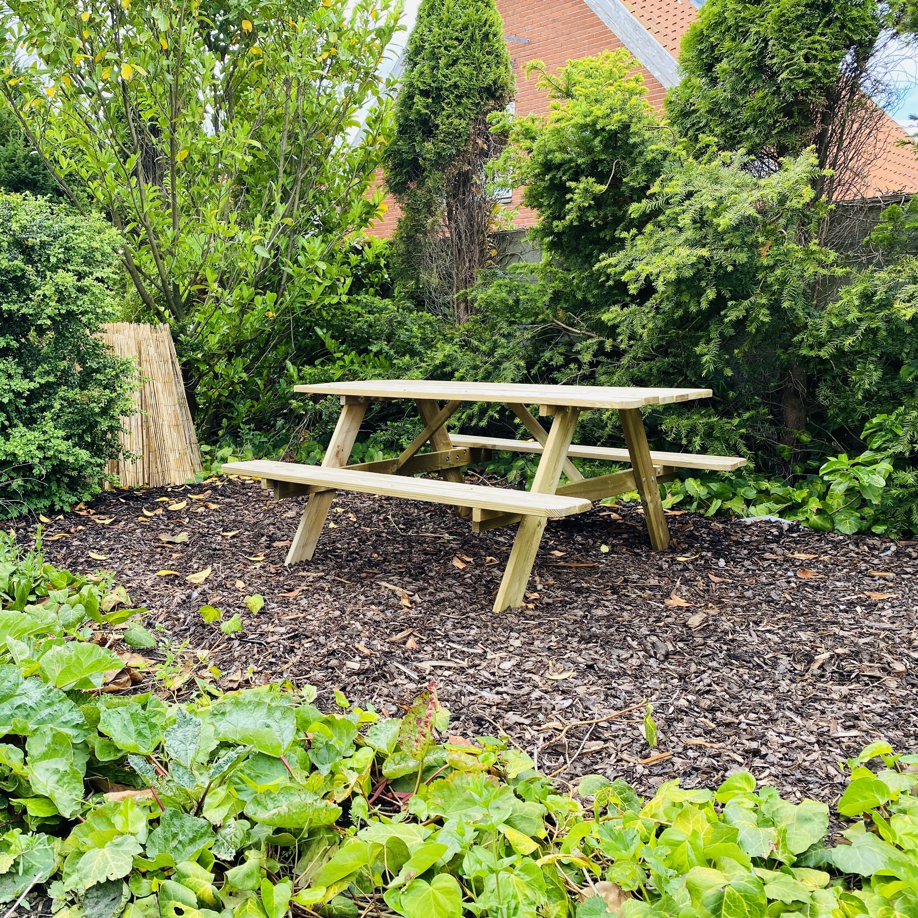 Una mesa de picnic de madera en un jardín con mantillo y diversas plantas verdes.