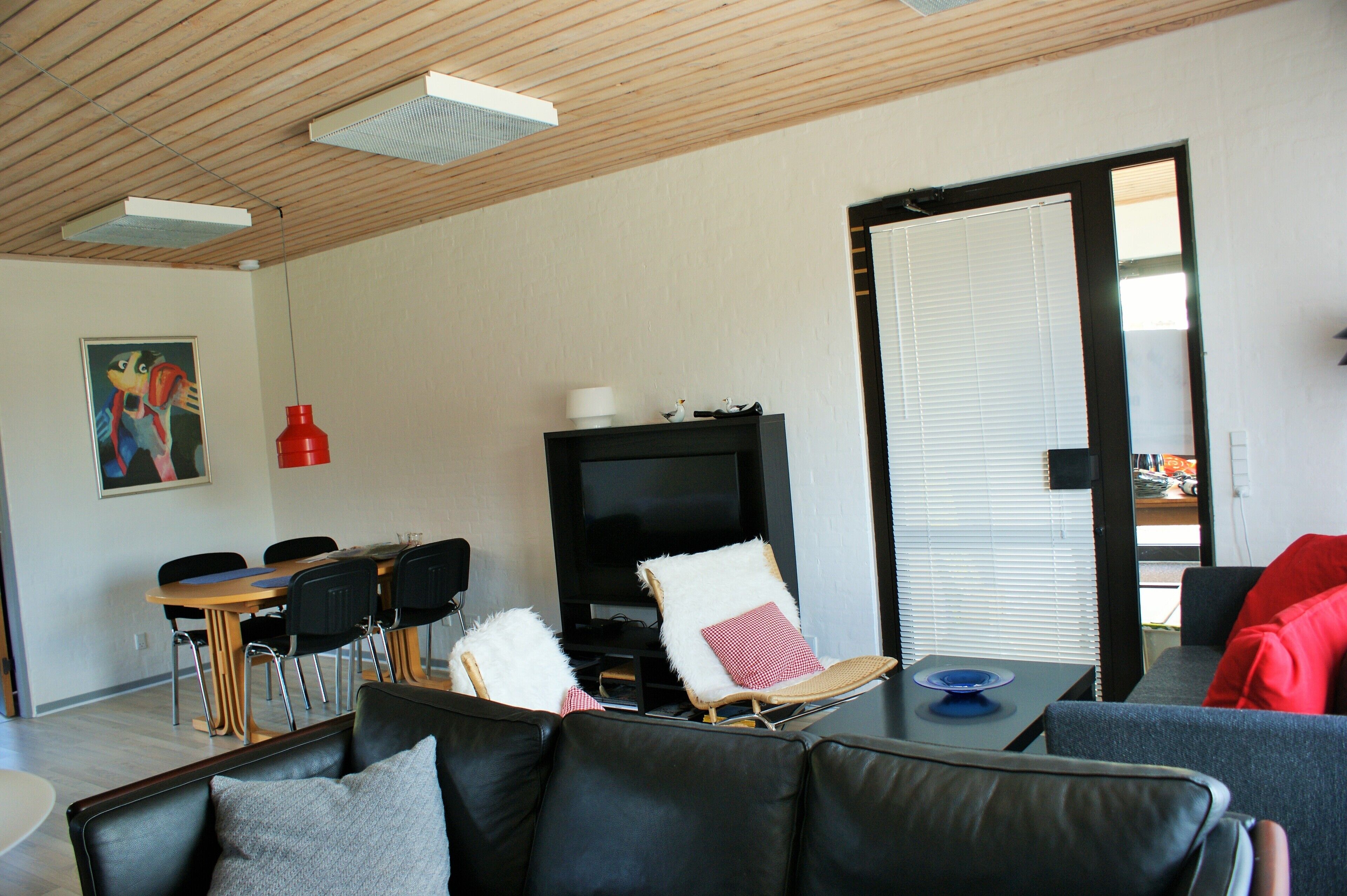 Una sala de estar moderna con techo de madera, un televisor de pantalla plana, una zona de comedor con sillas y un sofá con cojines.