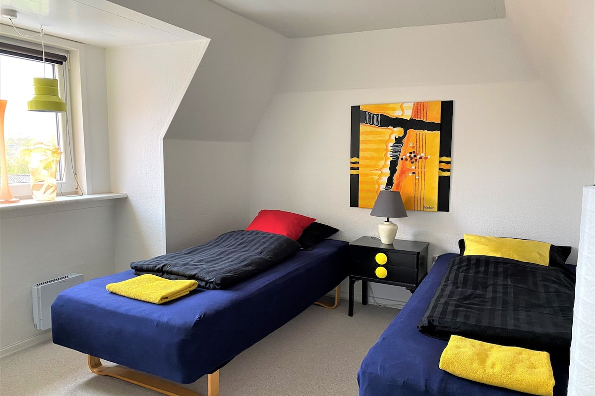 Ein Schlafzimmer mit zwei Einzelbetten, einem Nachttisch mit Lampe, einem Fenster mit Ausblick und einem Bild an der Wand.