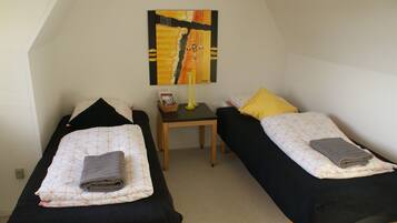 A room with two single beds, a small table, a lamp, and a painting on the wall.