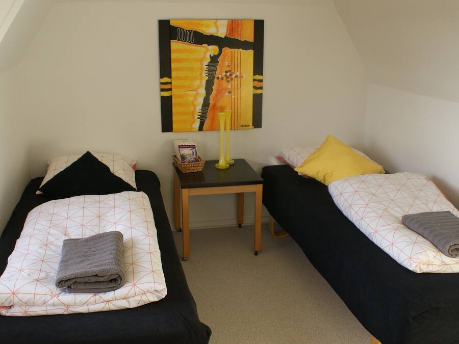 A room with two single beds, a small table, a lamp, and a painting on the wall.