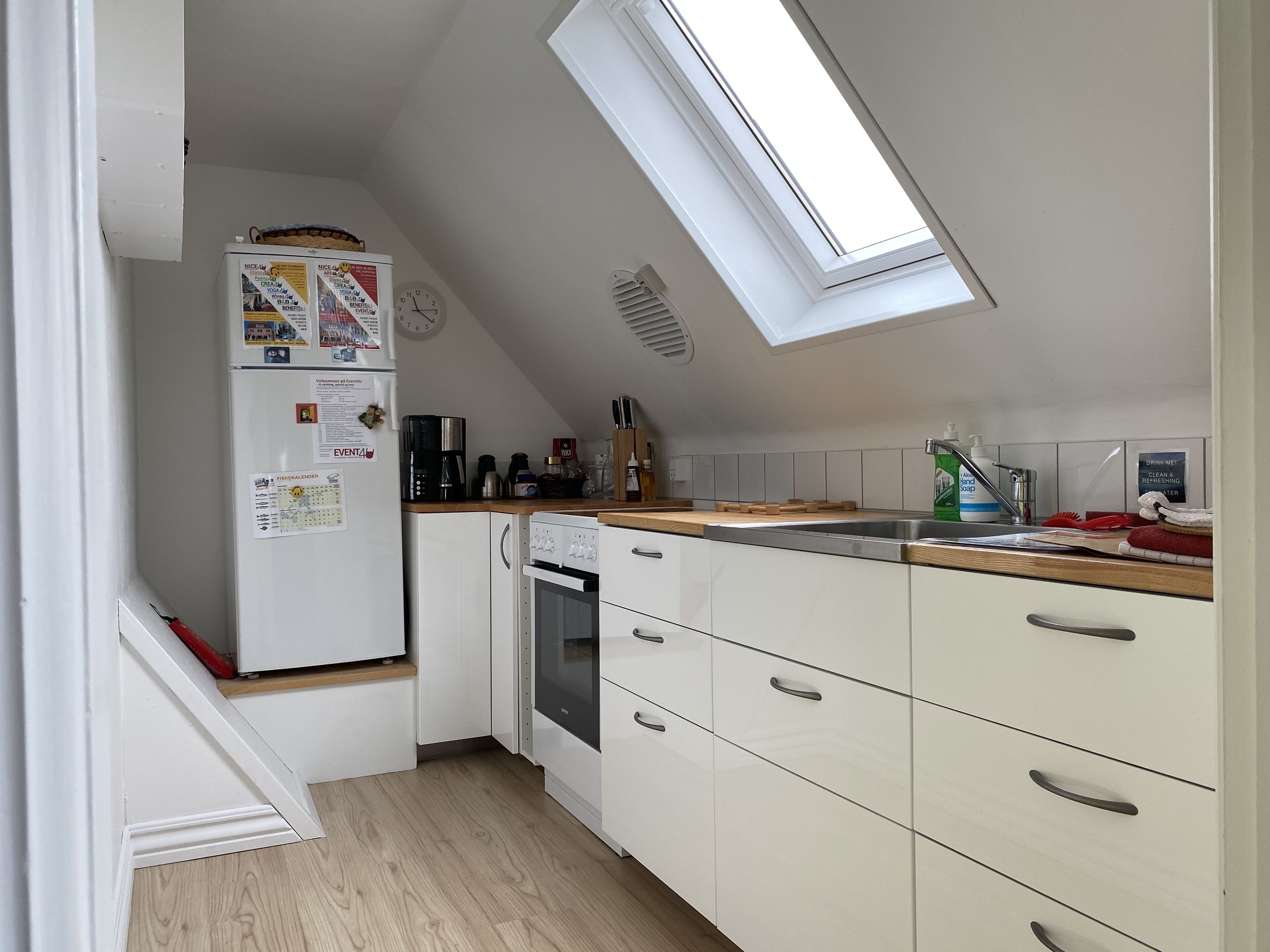 A compact kitchen with a refrigerator, coffee maker, oven, and a skylight.