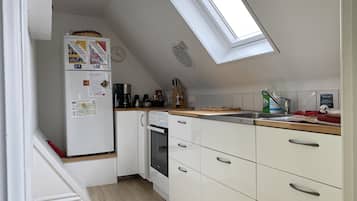 A compact kitchen with a refrigerator, coffee maker, oven, and a skylight.
