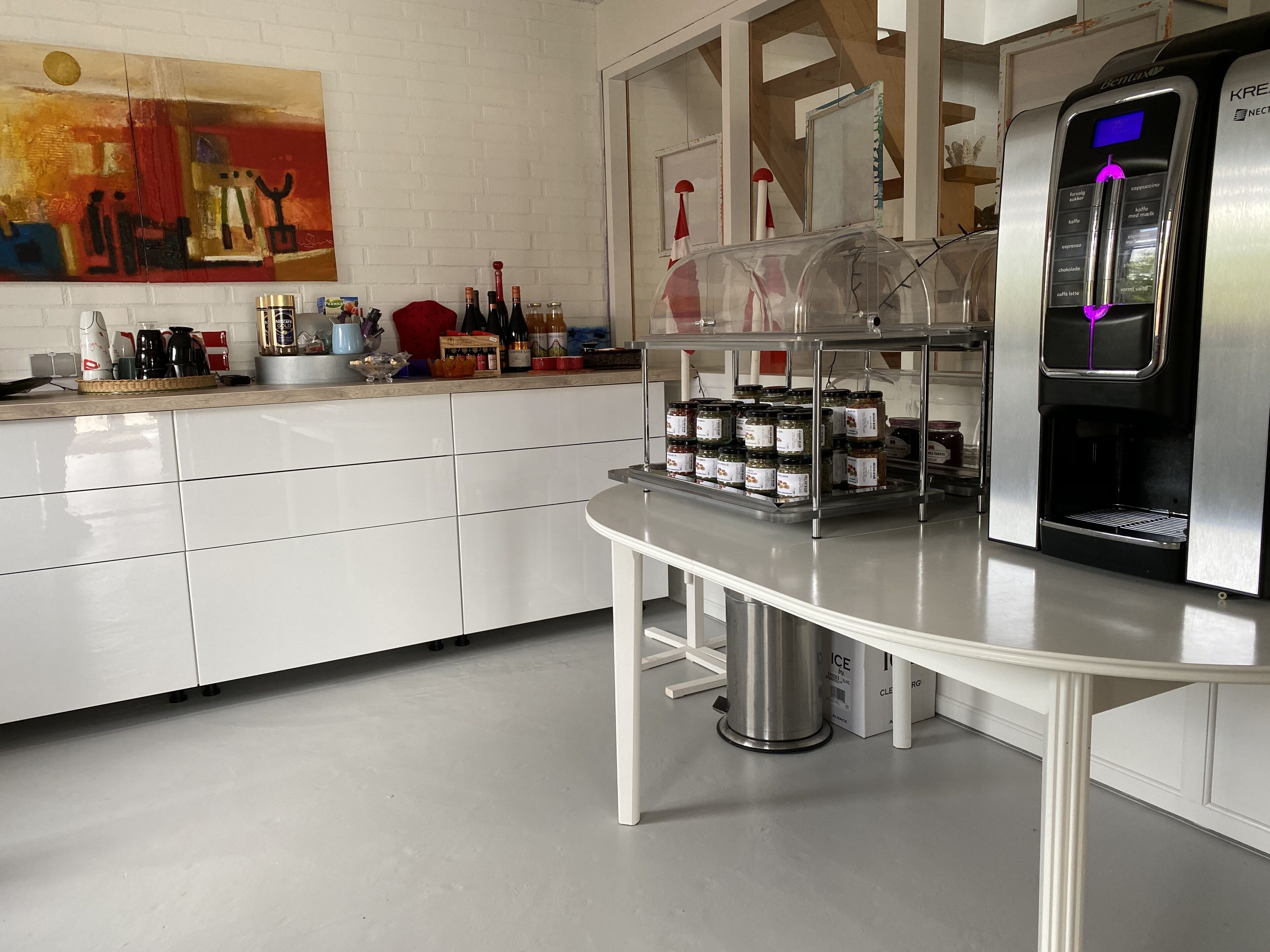 Een moderne keuken met een koffieapparaat, potten met kruiden en een schilderij aan de muur.
