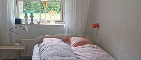 Un dormitorio con cama, mesita de noche, lámpara y ventana con cortinas.