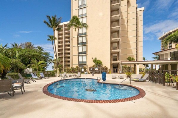A hotel with a swimming pool surrounded by lounge chairs and palm trees.