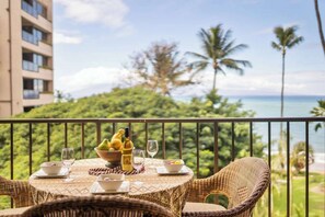 A dining table with a view of the ocean and palm trees.