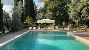 Una piscina rectangular con agua azul cristalina, rodeada por una terraza de madera y una fila de sillones blancos.