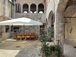Eine Terrasse im Freien mit Steinmauern, einem Holztisch und -stühlen sowie einem weißen Sonnenschirm.