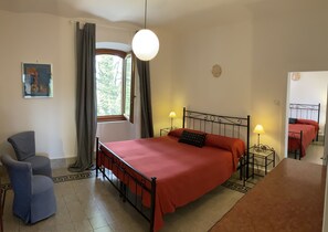 Ein Schlafzimmer mit Bett, Stuhl, Schreibtisch, Lampe und einem Fenster mit Vorhängen.