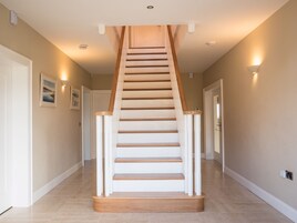 A modern staircase with wooden steps and white railings, leading to a landing with recessed lighting.