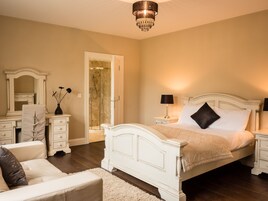A bedroom with a large bed, a nightstand, a dresser, a chair, and a walk-in closet.