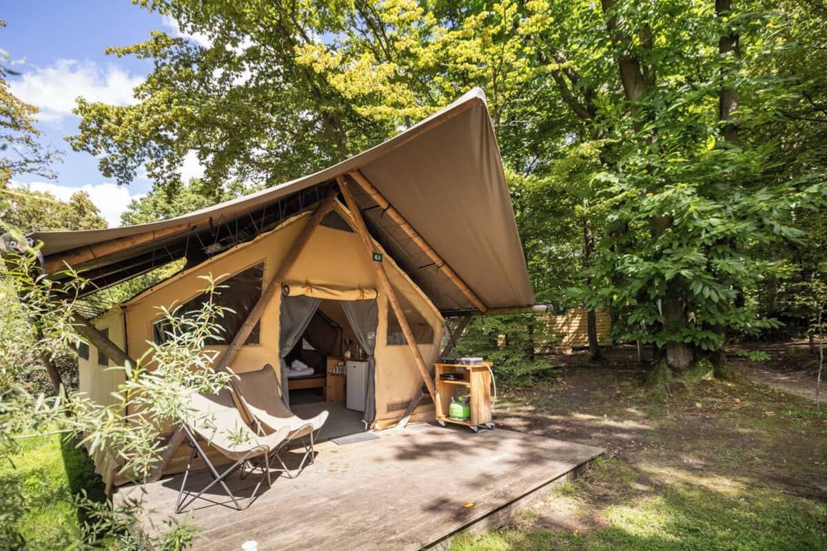 A tent with a slanted roof, a small kitchenette, and a wooden deck with a chair.