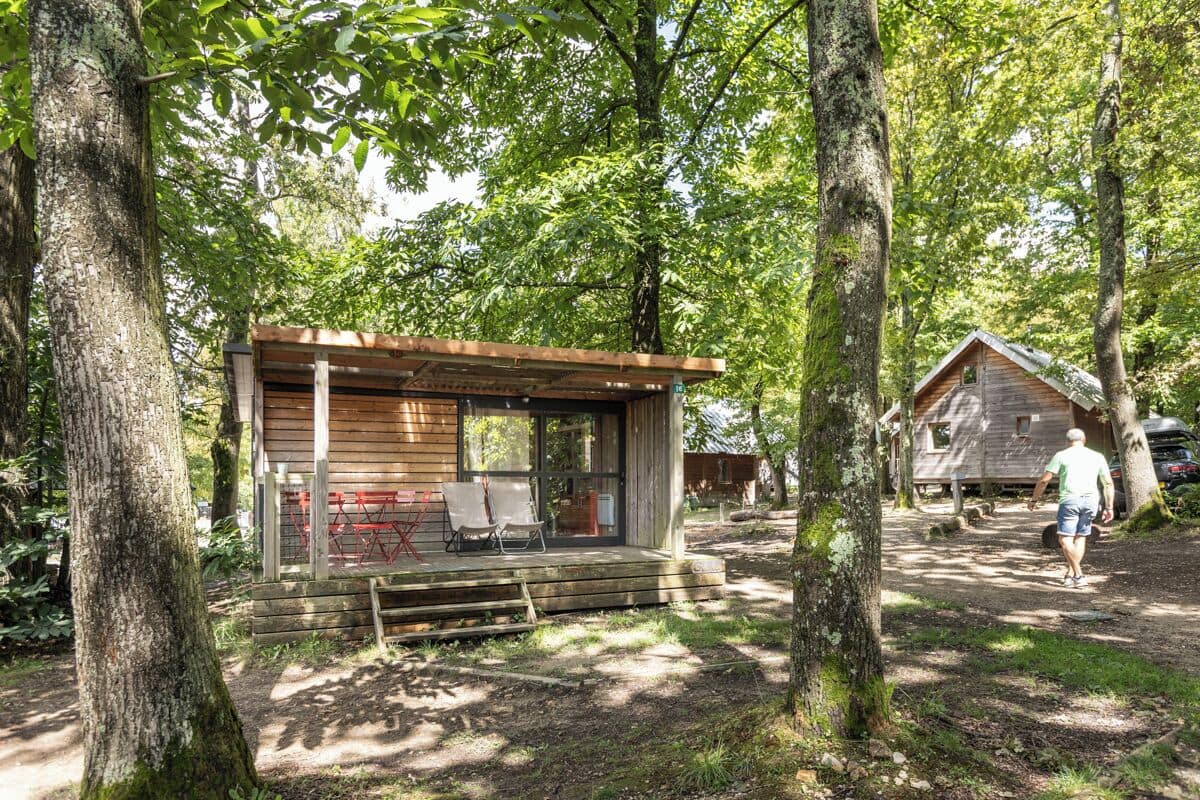 A rustic cabin with a wooden deck and a covered porch, surrounded by trees.