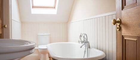 A bathroom with a freestanding bathtub, a toilet, and a window above the toilet.