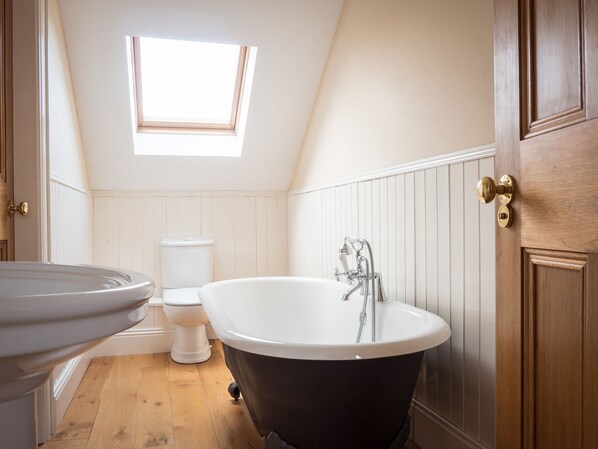 Une salle de bain avec une baignoire sur pieds, des toilettes et une fenêtre située au-dessus des toilettes.