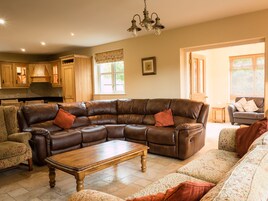 A spacious living room with a large sectional sofa, a wooden coffee table, and a kitchen area visible in the background.