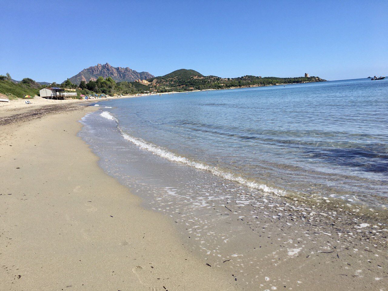 Una playa con agua cristalina, una orilla arenosa y una montaña al fondo.