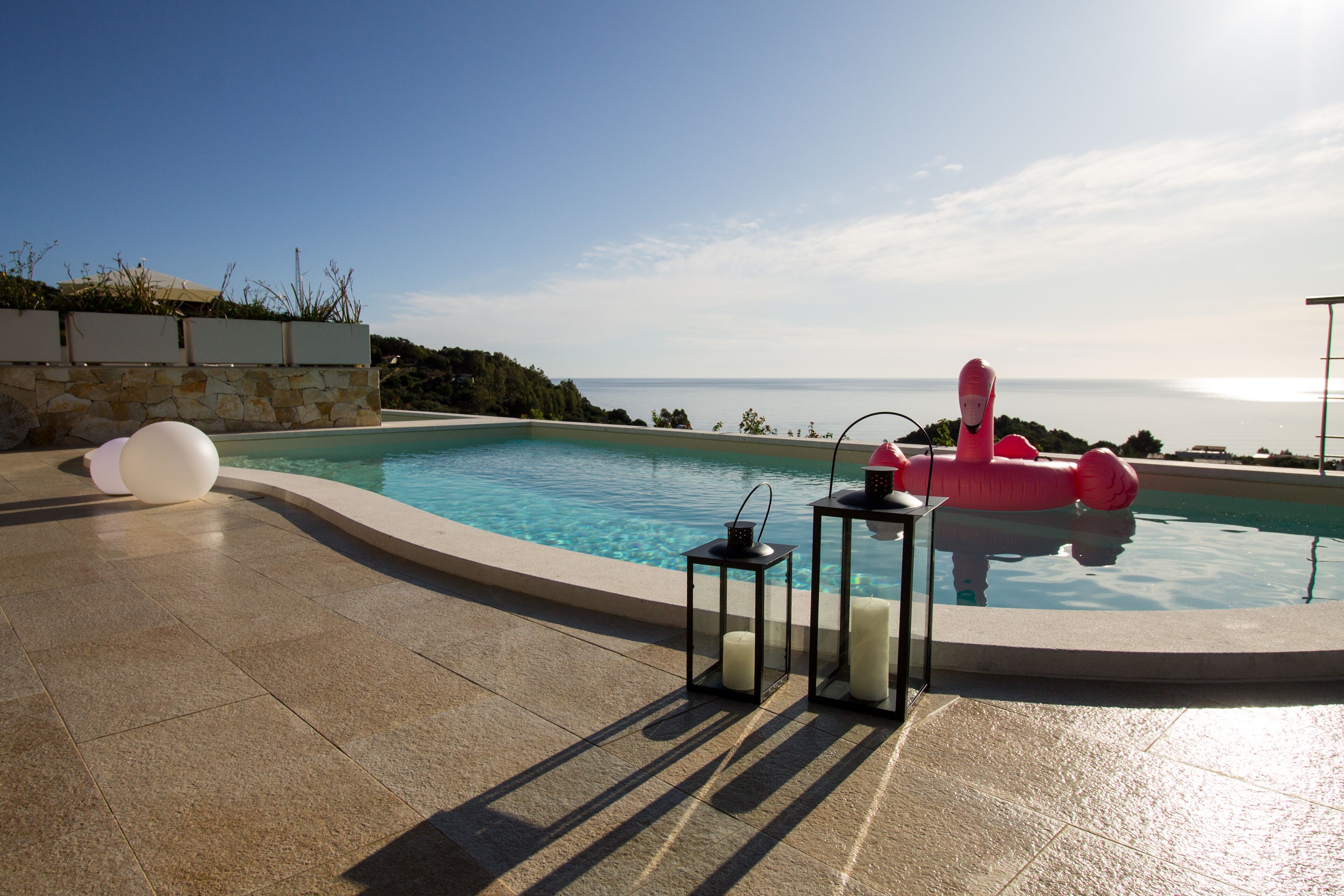 Una piscina con vistas al mar, un flotador inflable rosa y velas junto a la piscina.