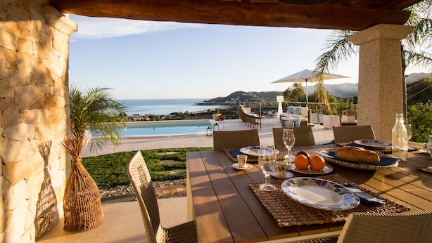 Un comedor con vista al océano, mobiliario exterior y una mesa lista para comer.