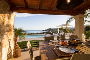 Un espace repas offrant une vue sur l’océan, avec des meubles d’extérieur et une table dressée pour le repas.