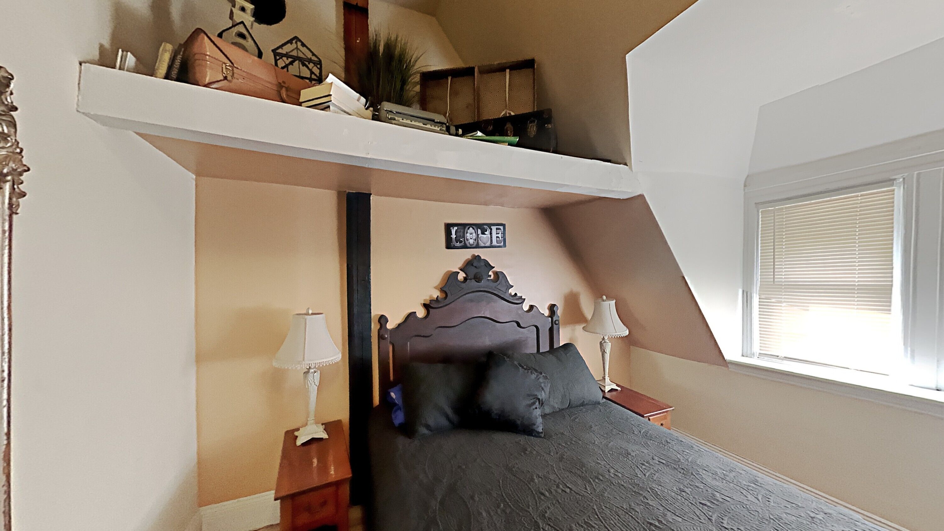 Een slaapkamer met een hoogslaper, een klein bureau en een raam met jaloezieën.