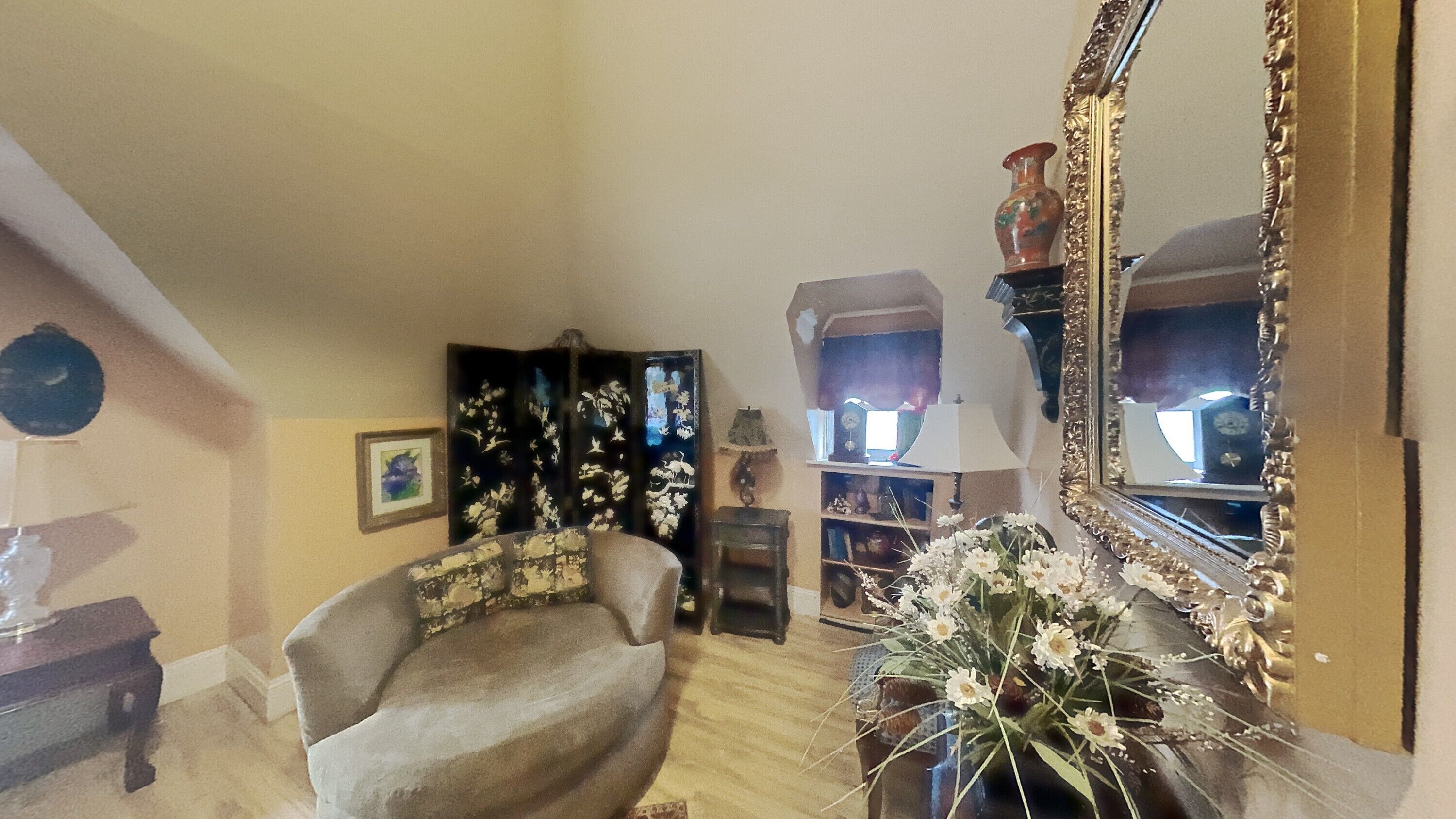 A cozy living room with a comfortable armchair, a large mirror, and a vase with flowers.