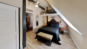 Une chambre à coucher comprenant un lit, un banc, un ventilateur de plafond et une petite table avec une lampe.