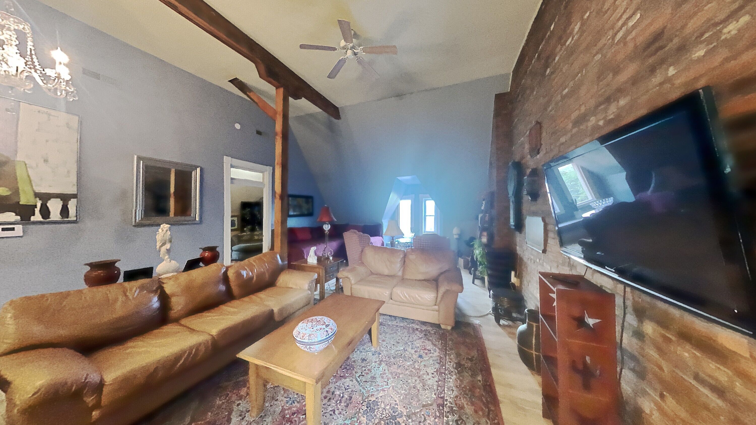 A living room with a large flat-screen TV, leather sofas, a wooden coffee table, and a ceiling fan.