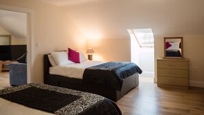 A bedroom with a bed, bedside table, lamp, dresser, and a TV. - The Apartment at Mullans Bay (Enniskillen)