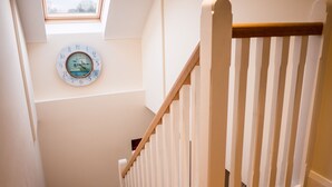 A staircase with a wooden handrail and a white railing, leading to a landing with a clock on the wall. - The Apartment at Mullans Bay (Enniskillen)