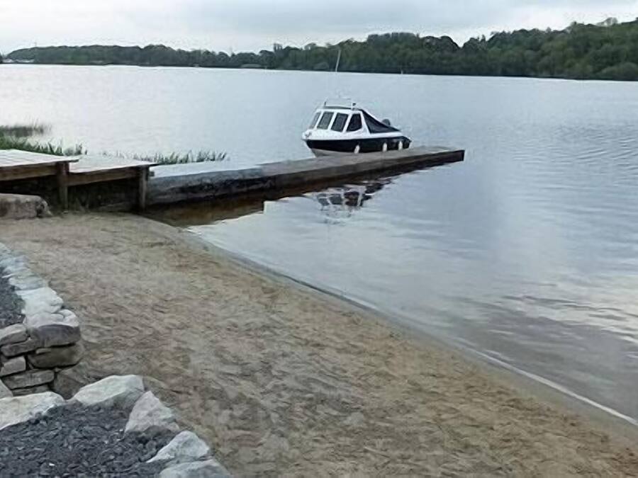 Un bateau était amarré sur un lac paisible, près d’une jetée en bois et d’un mur de pierres.