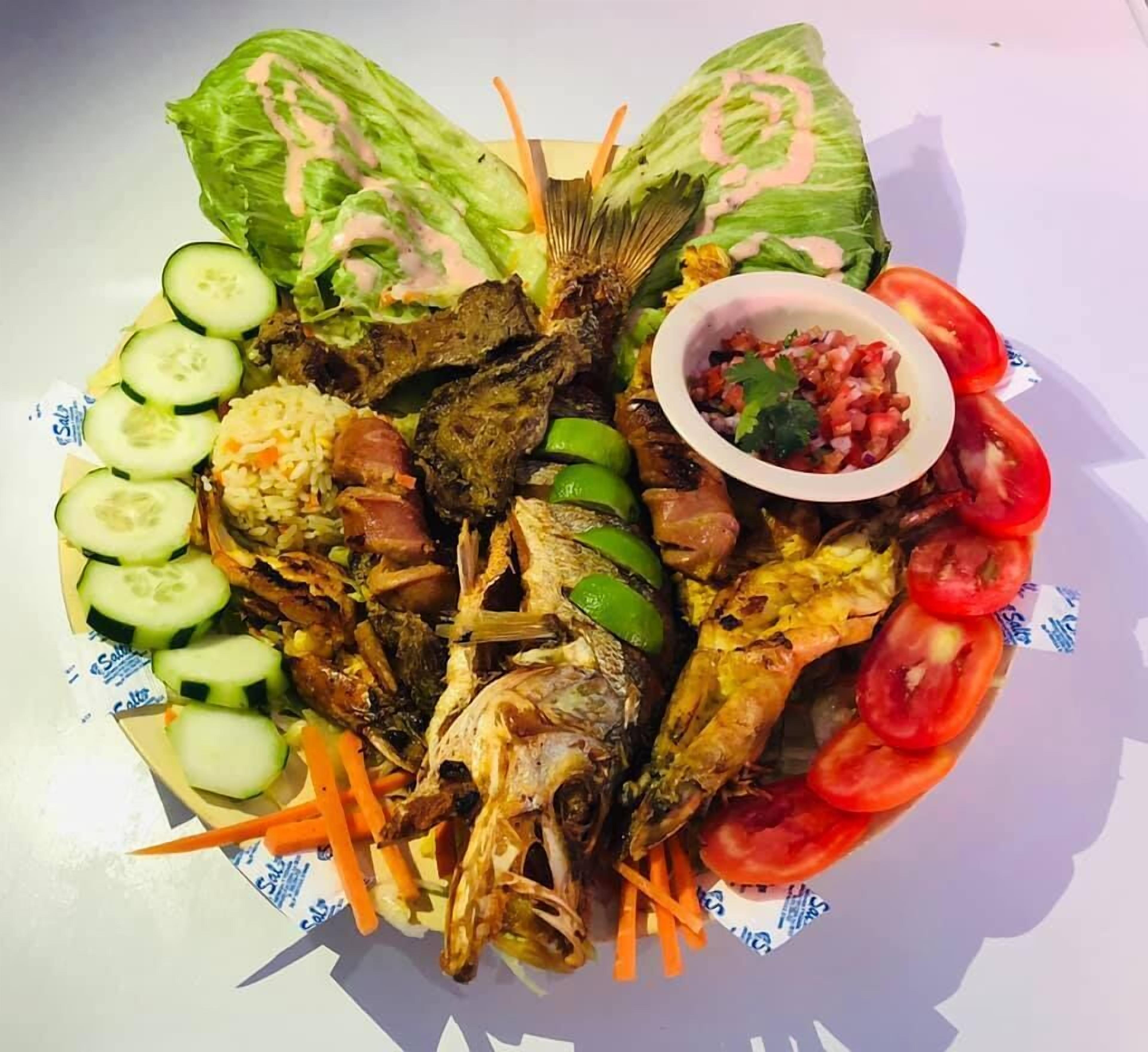 Um prato de comida com diversos itens, incluindo peixe, legumes e uma pequena tigela de salsa.