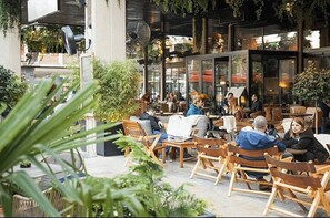 Un caffè all'aperto con sedie e tavoli di legno, immerso nel verde e circondato da architettura moderna.