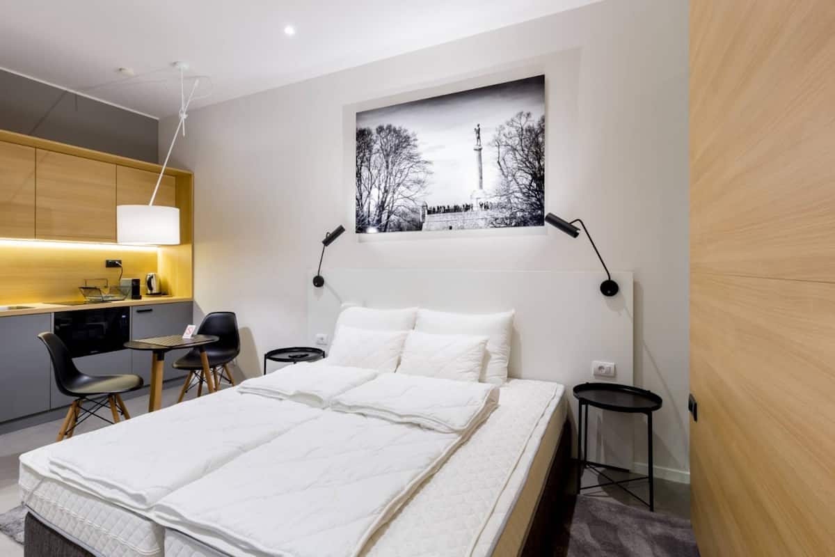 Ein modernes Hotelzimmer mit einem Bett, einem Schreibtisch, einem Stuhl, einem kleinen Tisch, einer Lampe und einem Bild an der Wand.