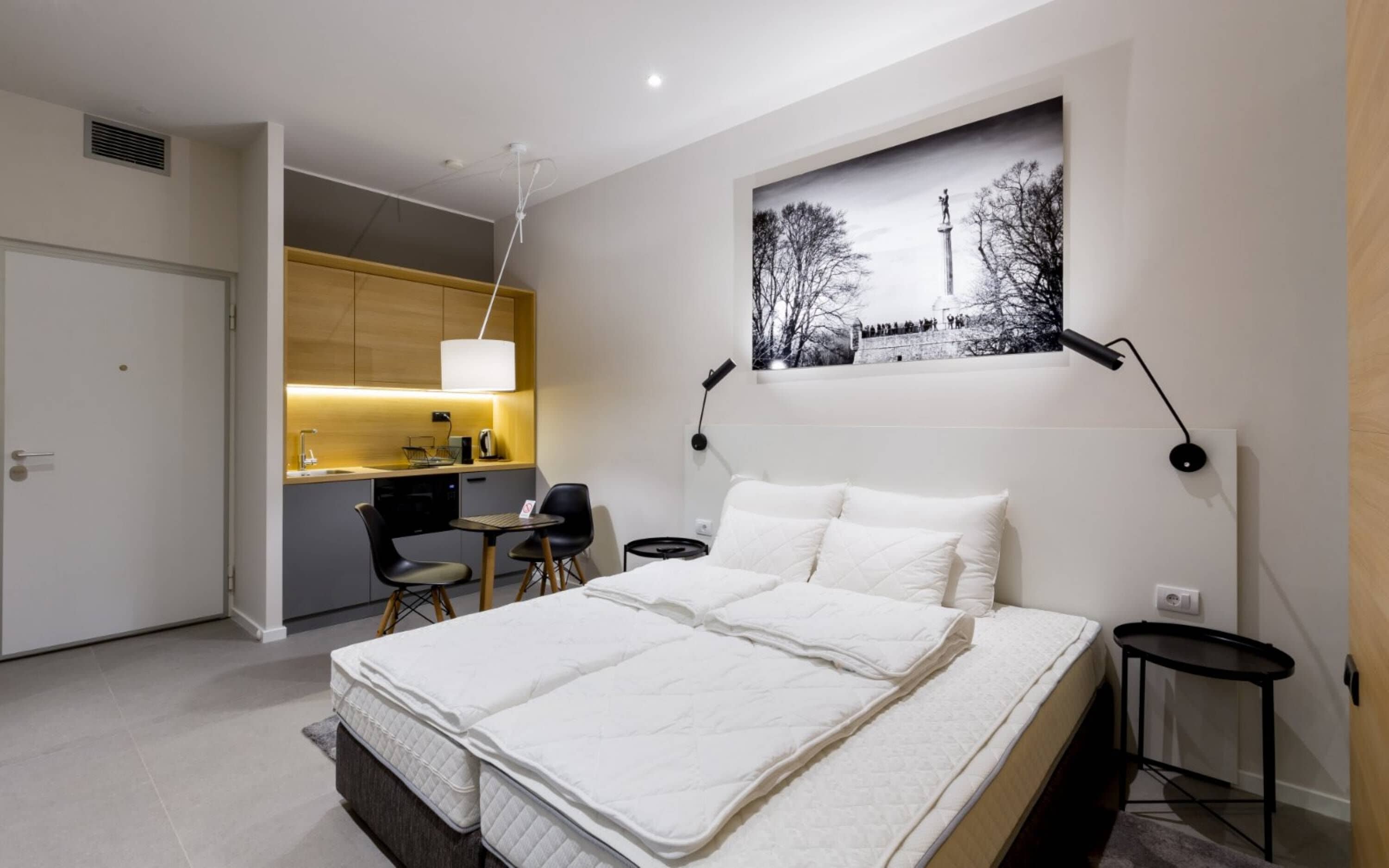 A modern hotel room with a bed, a small desk, a chair, and a dining area.