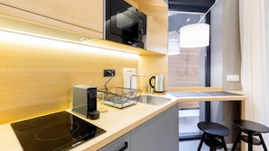 A modern kitchen with a built-in induction cooktop, a black microwave, a kettle, and a coffee maker. There are two stools and a small table. - Teanna Lux Apartments (Belgrade)