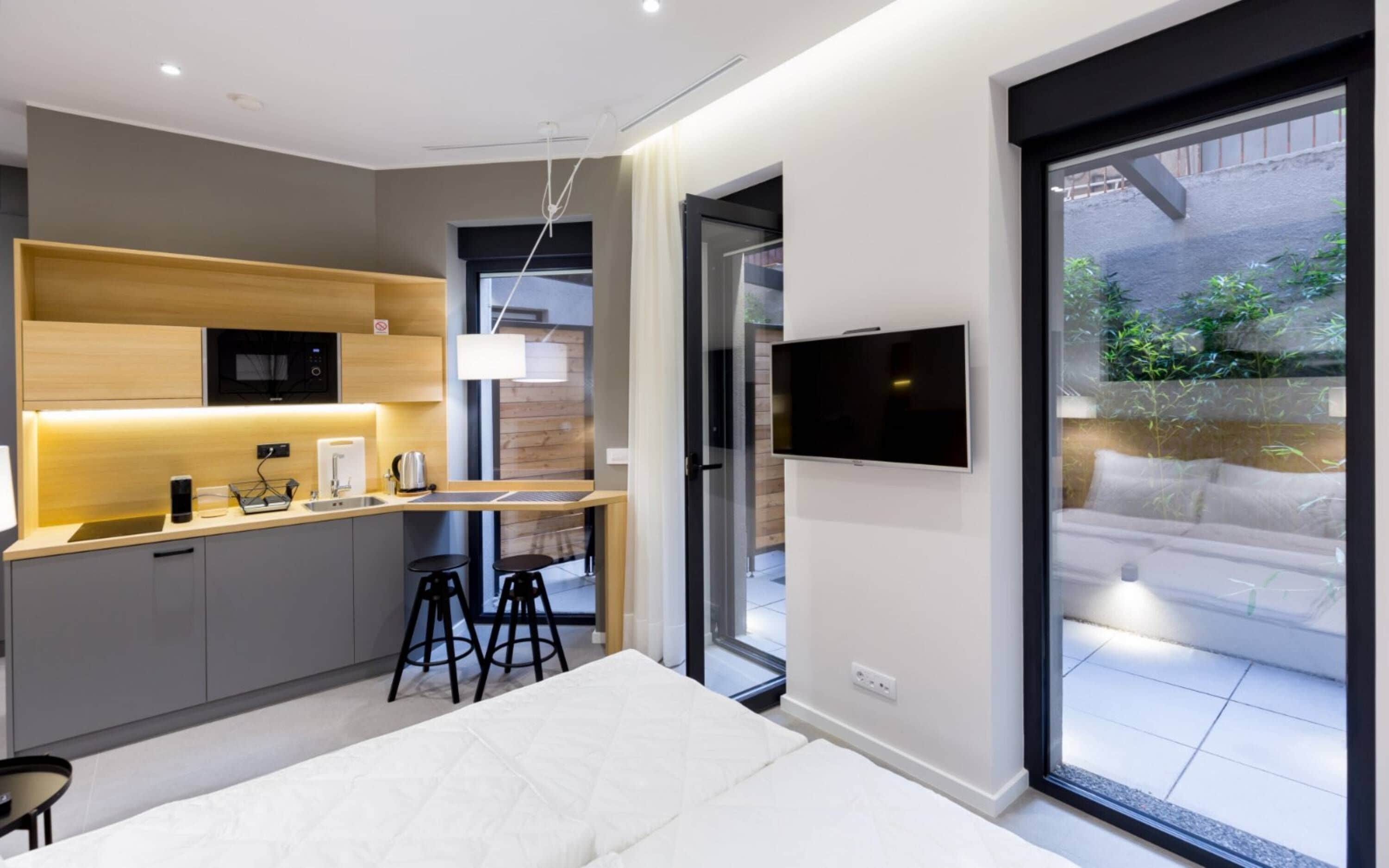 A modern kitchen with a built-in microwave, a coffee machine, and a sink. There is a dining area with a table and chairs, and a large window offering a view of the outdoors.