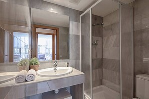 A modern bathroom with a large mirror, two sinks, a shower, and a view of the city.