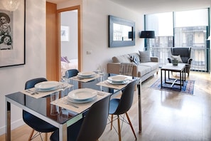 Un espace repas moderne avec une table en verre, des chaises et un canapé en arrière-plan.