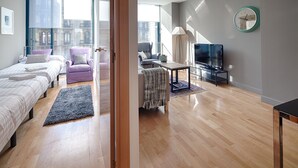 A modern hotel room with a large bed, two armchairs, a sofa, a TV, and a view of the city through large windows. - Pedrera Suites - Habitat Apartments (Barcelona)