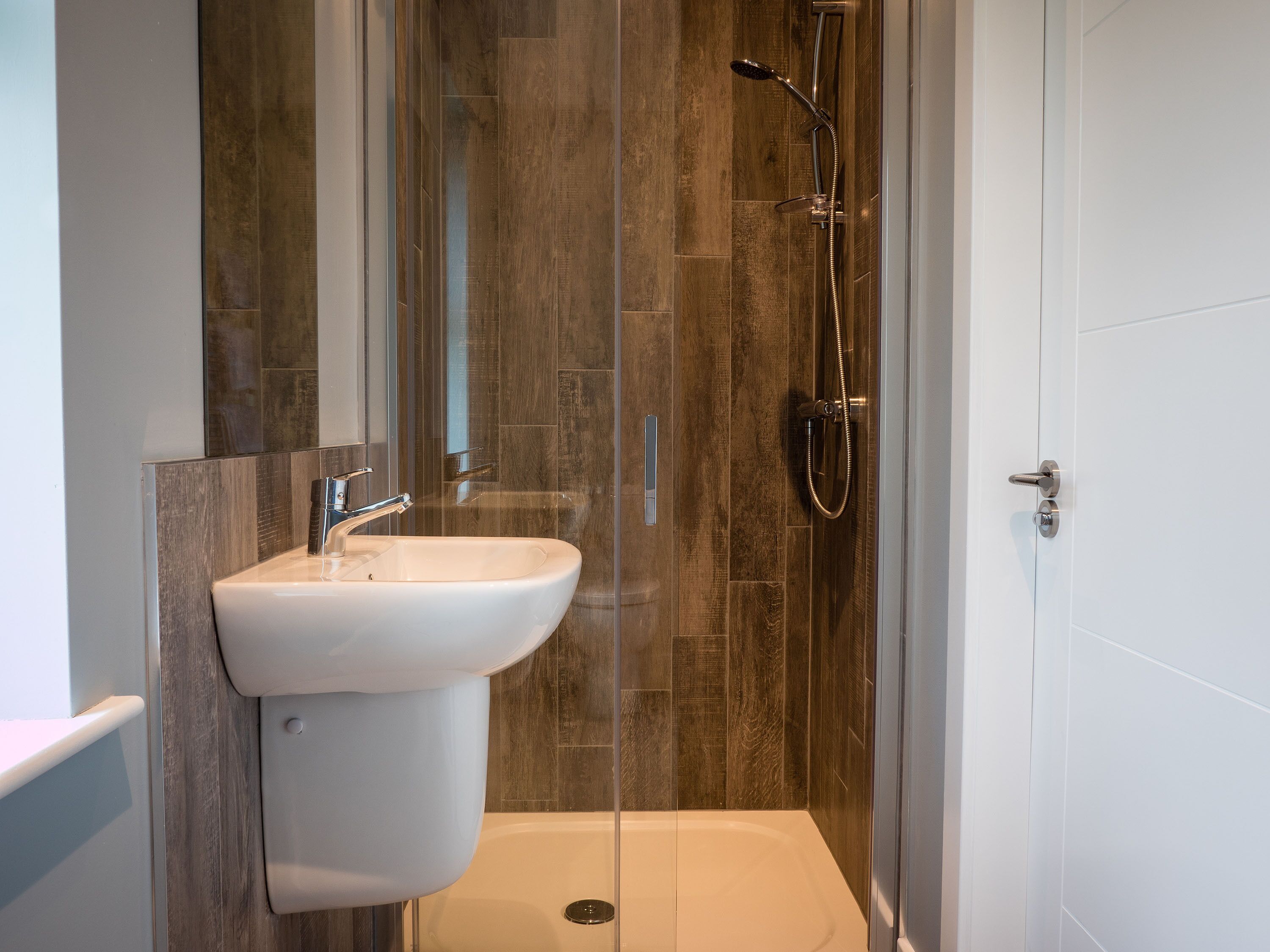 A modern bathroom with a glass shower enclosure, a white sink, and a wooden wall panel.