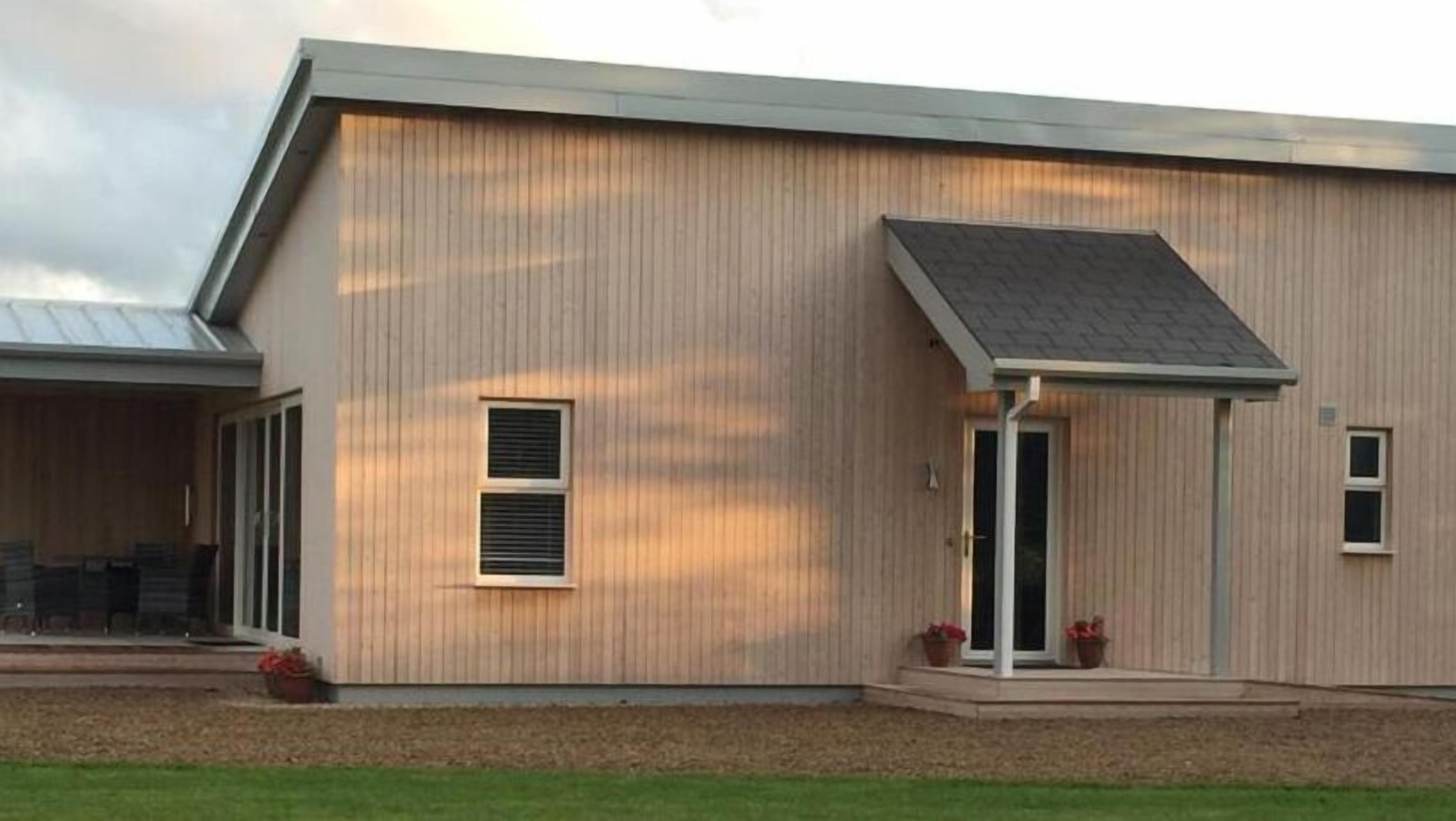 A modern two-story building with a flat roof, large windows, and a covered porch area.