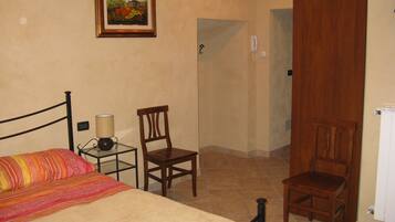 Una camera da letto con un letto, due sedie, un comodino con una lampada, un quadro appeso al muro e una porta che dà su un'altra stanza.