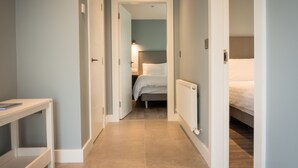 Een smalle gang met een bed aan het einde, een radiator aan de muur en een kleine tafel aan de linkerkant.