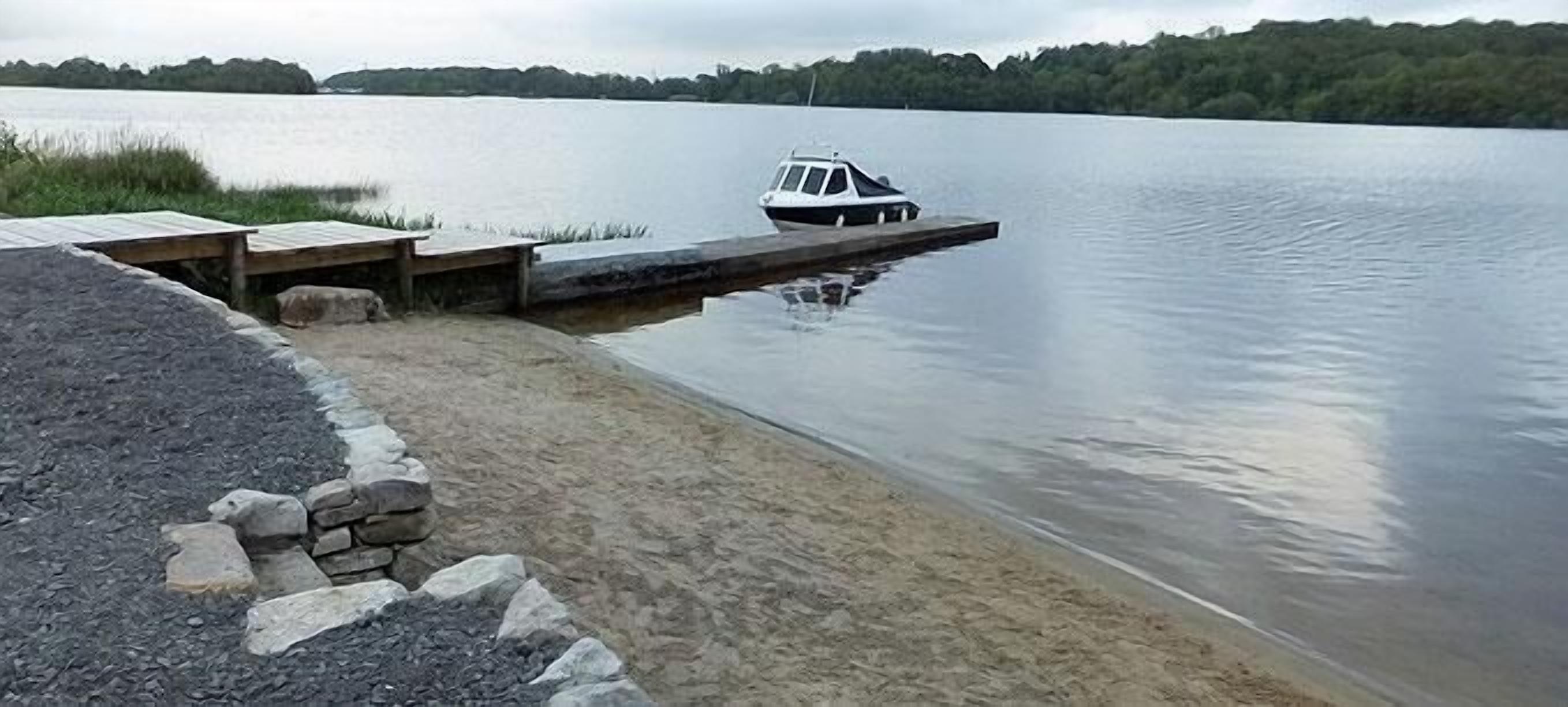 A boat docked at a calm lake with a wooden pier and a stone wall.
