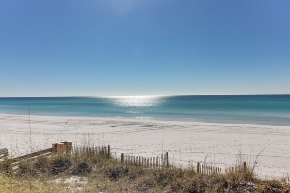 Enjoy a serene beach experience with a clear view of the sea, surrounded by natural vegetation and a wooden fence.
